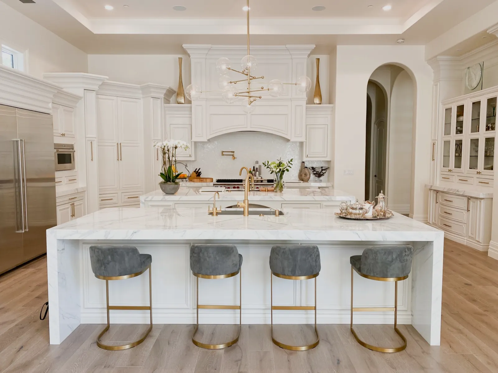 White estate kitchen with custom cabinetry, paneled range hood, and marble waterfall island
