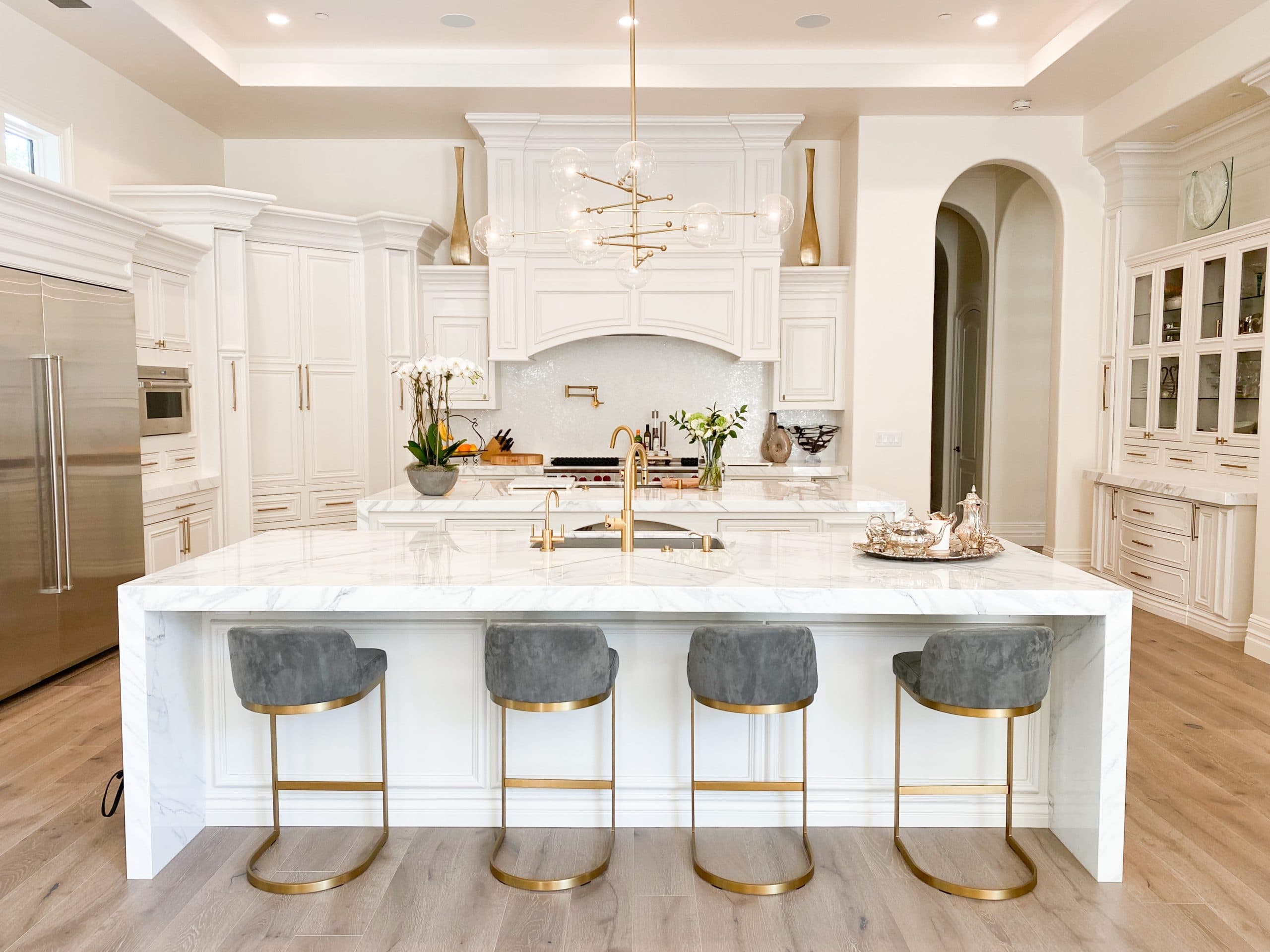 Estate kitchen with custom white cabinetry, paneled range hood, and a marble waterfall island